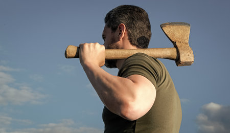 back view of guy with axe. lumberjack man hold ax. brutal man on sky background.