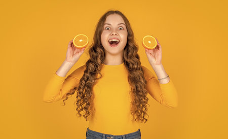 amazed teen girl hold orange fruit on yellow backgroundの写真素材