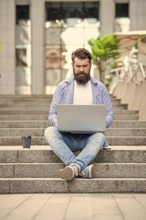 Serious freelancer typing on laptop sitting on stairs. Freelancer man using laptop for remote workの写真素材