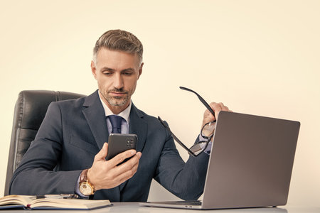 grizzled businessman with eyewear using phone in office with computerの写真素材