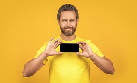 cheerful man showing smartphone app isolated on yellow. man showing smartphone app on background....