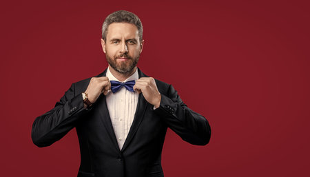 formal tuxedo man isolated on red background with copy space. tuxedo man in formal wear studio. tuxedo man with formal bow tie. photo of tuxedo man in formal suit.の写真素材