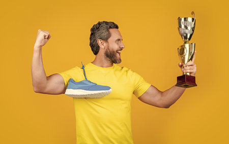 positive champion man hold award on background. champion man hold award in studio. photo of champion man hold award and sneakers. champion man hold award isolated on yellow.の写真素材