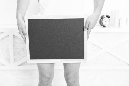 Blank blackboard as advertising. Guy crop view holding blackboard at level of genitals. Small black blackboard in frame. Writing board balcboard, copy space.の写真素材