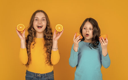 surprised teen girls hold orange fruit on yellow background.の写真素材