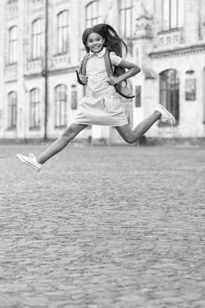 glad jumping school girl with backpack. jumping school girl outdoor. photo of jumping school girl. jumping school brunette girl.の写真素材