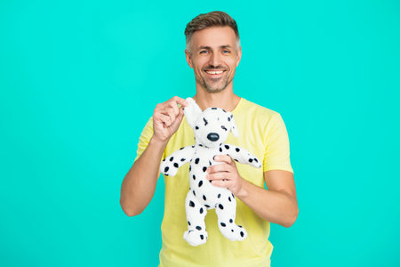 Man with toy isolated on blue. Childish habits. Caucasian man playing with toy. Playful mood. Optimistic mature man holding soft toy. Positive emotions.の写真素材