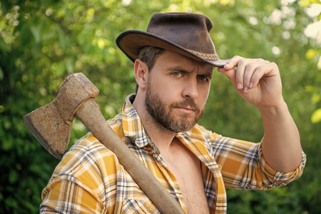portrait of cowboy with axe wearing checkered shirt. cowboy with axe outdoor. photo of cowboy with axe. cowboy with axe.の写真素材