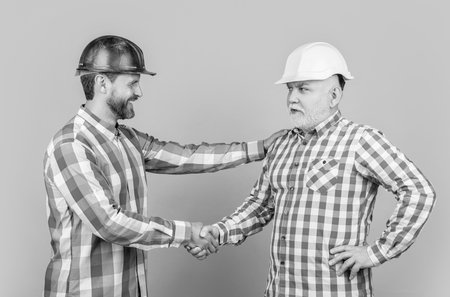 cheerful partners men handshaking on background. photo of partners men handshaking wear building helmet. partners men handshaking isolated on yellow. partners men handshaking in studio.の写真素材