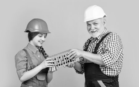 happy girl and grandfather bricklayer in helmet on yellow background.の写真素材