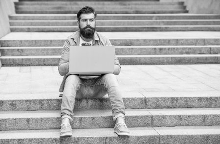full length of freelancer man has communication on laptop. freelancer man has communication on pc outdoor. communication of freelancer man outside. freelancer man has communication at coffee break.の写真素材