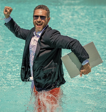 successful man. Businessman in suit with laptop in swimming pool. business man on summer vacation. businessman in wet suit in swim pool. Remote working. Summer business dreams. Fun business lifestyle.の写真素材