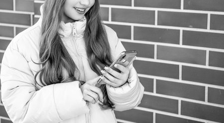 cropped view of teen girl messaging on phone outdoor. teen girl messaging on phone wearing hat. photo of teen girl messaging on phone outside. teen girl messaging on phone at brick background.の写真素材