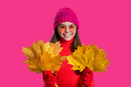 Happy young girl playfully hold yellow maple leaves. Teen girl with fallen leaves isolated on pink....