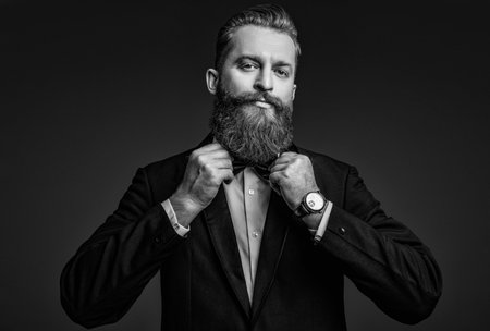Male accessory. Gentleman in tuxedo bowtie has luxury watch. Expensive time wrist watch. Man in tuxedo adjusting bowtie and watch. Elegant watch accessory. Time. Elegant gentleman isolated on greyの写真素材