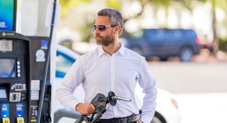 Businessman refueling luxury car hold filling gun at gas station. Businessman in sunglasses...