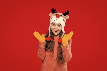Childhood lifestyle. Winter child wardrobe. Teenage girl in Xmas hat isolated on red. Winter fashion for teenage style. Girl in knitted hat in winter season. Earflap comfortの写真素材