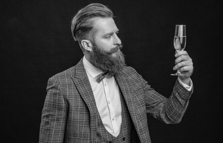 Elegant man in formal wear hold glass of champagne isolated on black. Celebrating success. Cheers. Bearded man with formal look. Celebrate with champagne. Cheering and celebrating.の写真素材
