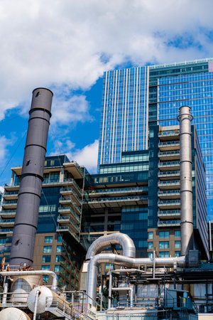 Steam plant. Industrial facility with factory pipe. Environmental pollution. Industry urban area. Industrial zone with steam plant. Urban facility factory with skyscraper on backgroundの写真素材