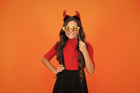 Girl devil has Halloween party props. Happy Halloween. Girl devil ready for Halloween party isolated on orange. Trick or treat. All Hallows party celebration. Hallows funny propsの写真素材
