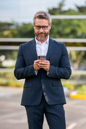 Mature Hispanic business man with phone. Business fast communication. Messaging and texting. Business man chatting on phone outdoor. Businessman using phone. Man phone chat in suitの写真素材
