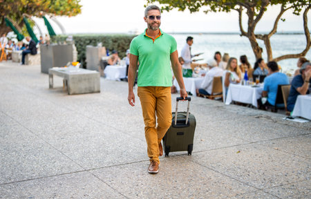 Traveler enjoy summer trip. Hispanic tourist traveler walking on city street. Tourist with suitcase. Man 40s traveler. Tourist on summer vacation. Traveler luggage for vacation trip. Summer tourの写真素材