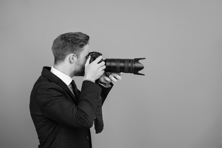 Freelance photographer. Photojournalist in business suit. Business photographer with camera. Journalist man taking photo isolated. Paparazzi photographer. Businessman hold photo camera. Copy spaceの写真素材