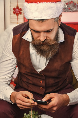 Bearded man in retro suit and Santa Claus hat writing phone greeting message for Christmas holiday or having shopping onlineの写真素材