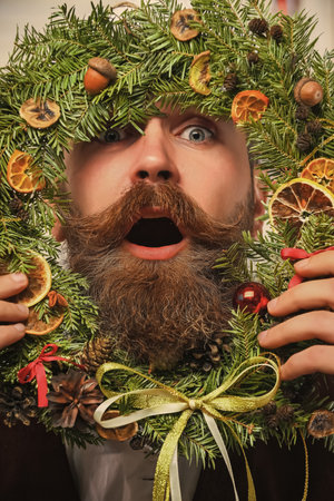 Xmas decoration for home. Decorated Christmas man. Bearded man at Christmas. New Year holiday. Man with moustache holding Xmas wreath. Happy New Year. Christmas wreath decorationの写真素材
