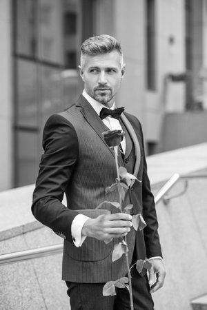 elegant man in black tuxedo. man wearing tuxedo bowtie outdoor. charismatic tuxedo man with red roseの写真素材