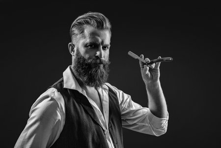 Bearded hipster barber isolated on black. Man beard haircut by hairdresser at barbershop. Handsome barber using retro blade while cutting hair. Modern barbershop haircut. Stylish haircutの写真素材