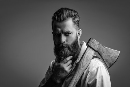 Bearded man holding an axe. Hair and beard care. Handsome bearded man. Beard styling. Brutal Caucasian hipster with moustache. Bearded man isolated on grey. Vintage barbershopの写真素材