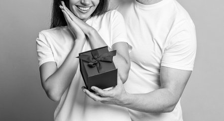 Loving man giving present for Valentines day. Gift box to surprised woman. Girlfriend receiving present from boyfriend. Valentines day couple. Couple in love. Womens day gift. Cropped viewの写真素材