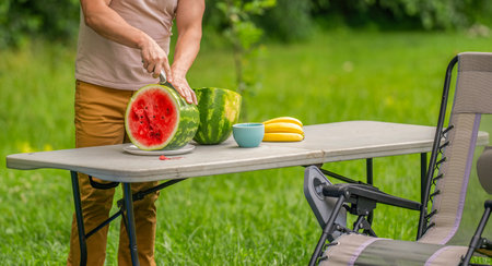 Man cutting watermelon. Picnic guy with watermelon outdoor in summer camp. Man eating yummy watermelon. Cropped man eat fruit. Man enjoying juicy fruit vitamin. Yummy camping, copy spaceの写真素材