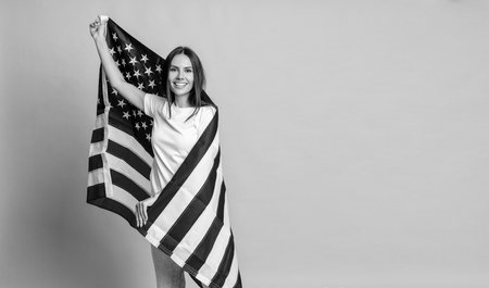 American Memorial Day or July 4th. Woman covered with American flag isolated on yellow. Flag of USA. National flag of united states on woman. Independence day. Patriotic happy woman. Copy spaceの写真素材