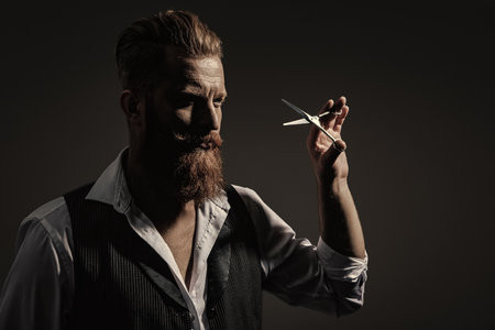 Man beard haircut by hairdresser at barbershop. Handsome barber using scissors while cutting hair. Modern barbershop haircut. Bearded hipster barber isolated on black.の写真素材