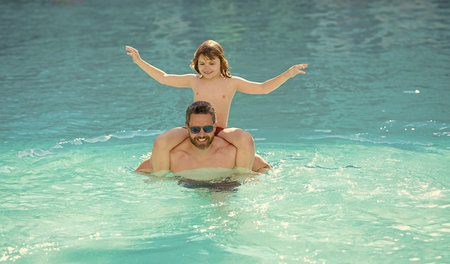 Happy family of father and son having fun in swimming pool at summer vacation outdoor
