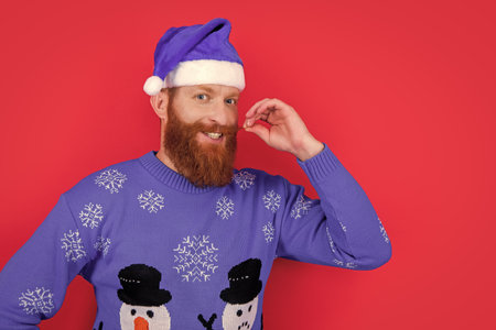 caucasian happy man in christmas sweater and santa hat isolated on red background with copy space.