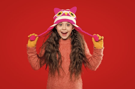 Teenager girl in a winter warm hat isolated on red. Happy girl in winter hat. Winter fashion style....
