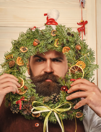 Happy New Year. Christmas wreath decoration. Xmas decoration for home. Decorated Christmas man. Bearded man at Christmas. New Year holiday. Man with moustache hold Xmas wreathの写真素材