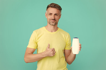 Man hold aftershave unbranded product or shampoo for haircare and skincare isolated on blueの写真素材