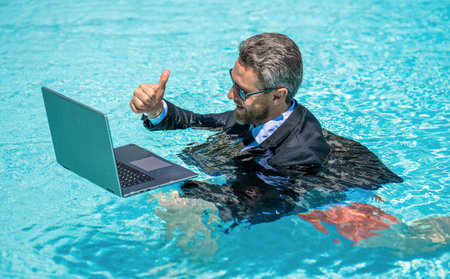 Freelance man has online video call. Freelance working online. Man using laptop for freelancing in swimming pool. Business freelancing. Businessman on summer vacation. Businessman on video conferenceの写真素材