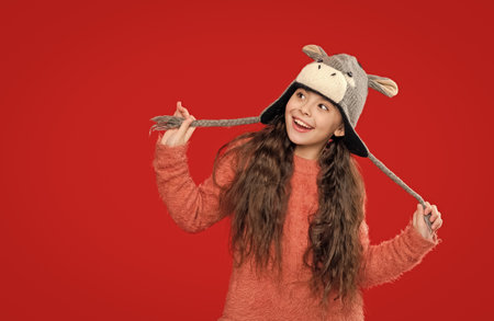 Outdoor lifestyle fashion. Teenager girl in a winter warm hat isolated on red. Happy girl in winter hat. Winter fashion style. Teenager knitted fashion. Childhood innocenceの写真素材