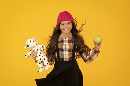 School happy teen girl student in stylish uniform and autumn hat holding toy with apple isolated on...