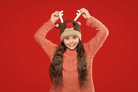 Winter fashion for teenage style. Girl in knitted hat in winter season. Childhood lifestyle. Winter child wardrobe. Teenage girl in Xmas hat isolated on red. Earflap detailingの写真素材