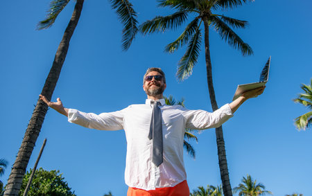 Online freelance work. Businessman boss with laptop. Business man using laptop near palm tree. Successful business trip. Man freelance work online at beach. Businessman on summer vacationの写真素材