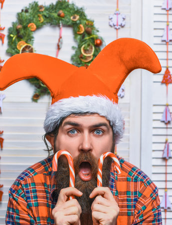 Amazed Santa Claus bearded man in Christmas hat hold candy cane stick during celebration of happy new year 2025の写真素材
