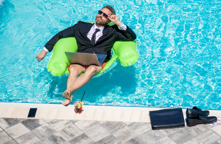 Freelance working online. Man using laptop for freelancing in swimming pool. Business freelancing. Businessman on summer vacation. Businessman on video chat. Freelance man has online video callの写真素材