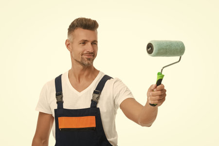 Man painter hold painting roller. Paint roller for decorator. Renovation work. Decorator man do renovation painting. Man renovator isolated white. Renovating painter. Selective focus. Home renovatorの写真素材