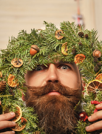 Christmas wreath decoration. Xmas decoration home. Decorated Christmas man. Bearded man at Christmas. New Year holiday. Man with moustache hold Xmas wreath. Happy New Year. Joyful Christmas spiritの写真素材